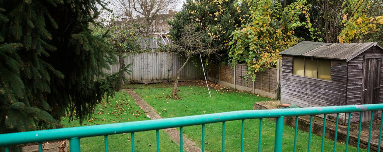 Elongated grassed back garden, directly down the centre is a paved walkway and a flattened raised concrete slab has been made to house a wooden shed.