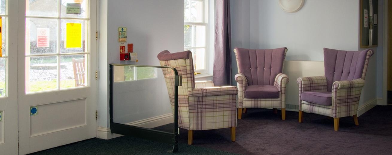 A cosy nook of a seating area of three regal lilac checked armchairs surrounding the long, tall window overlooking the garden area.