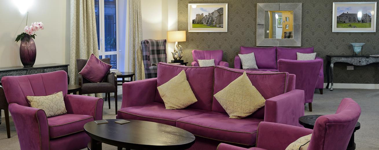The multiple purple sofas and arm chairs are the main focus point of the room adding vivid colour. The perimeter of the room are dress with ornate tables with elaborate vases.