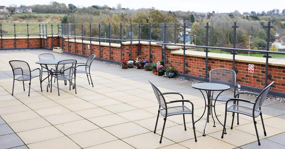 The balcony rooftop terrace is a patioed area with potted plant decoration, it has a few metal outdoor garden furniture table and chairs. With views over the local area.
