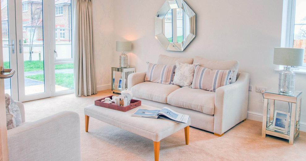 The generous living room is decorated neutrally with a three-seater cream fabric sofa with three push decorative cushions two in a pale pink and blue stripes and the centre one in cream with a soft silver floral pattern. The matching armchair sits opposite the sofa separated by a footstool being used as a coffee table with a wooden tea tray with tea making facilities ready for use. The mirrored side tables sit either side of the sofa decorated with large glass and cream lamps on top and picture frames on the bottom shelf. A hexagonal mirror complementing the side tables sits above the sofa. The room also has a patio door access straight into the garden area.