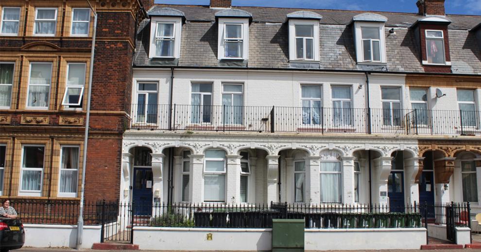 Ornate exterior of a three-storey whitewashed terraced supported housing property in Great Yarmouth. With second storey property width balcony.