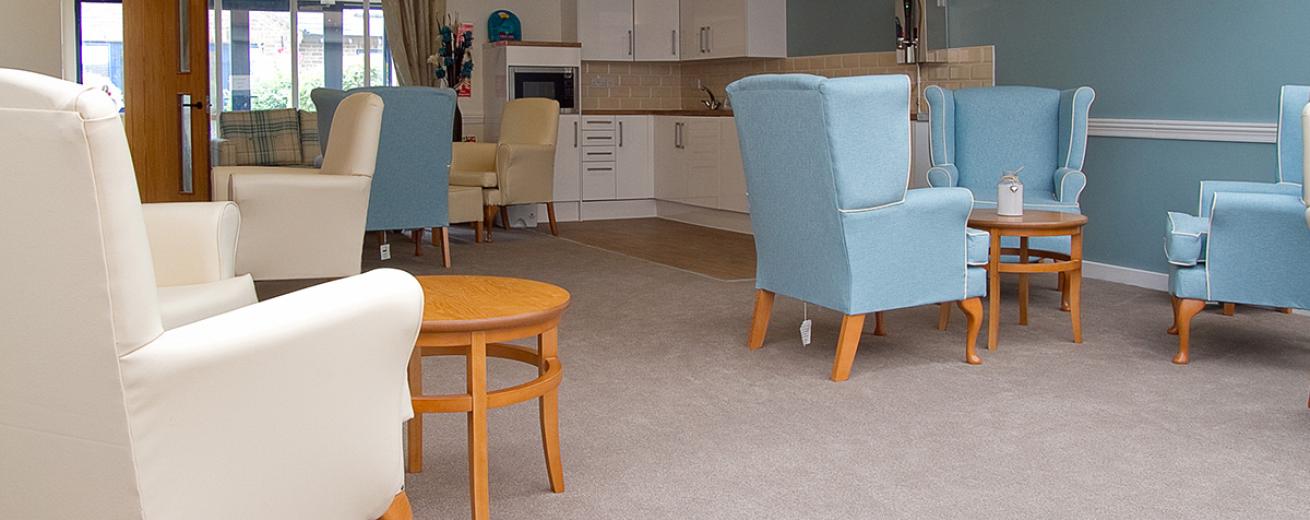 A cosy seating area, home to light blue and cream leathered armchairs with small circular wooden coffee tables. In the corner of the room is a small white kitchenette area, with built in microwave.