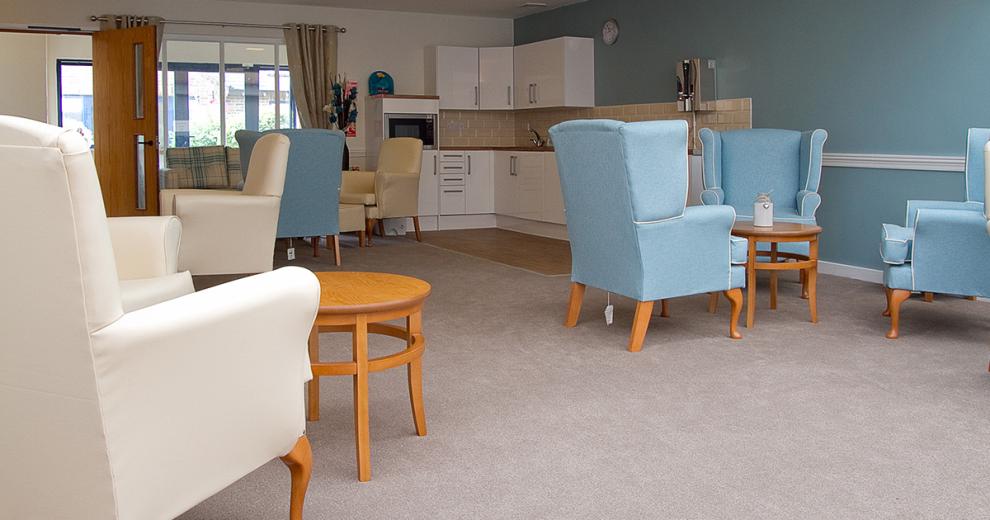 A cosy seating area, home to light blue and cream leathered armchairs with small circular wooden coffee tables. In the corner of the room is a small white kitchenette area, with built in microwave.