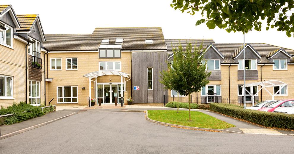 A modern two storey property built with yellow brick and a wooden panelling in random locations on the exterior of the property. The entrance has a covered walkway and dropped curb access.
