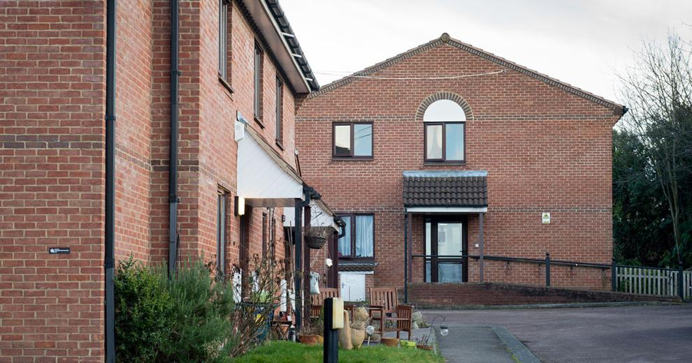 Single storey brick built residential care home, built on a corner plot with outdoor wooden dining set.