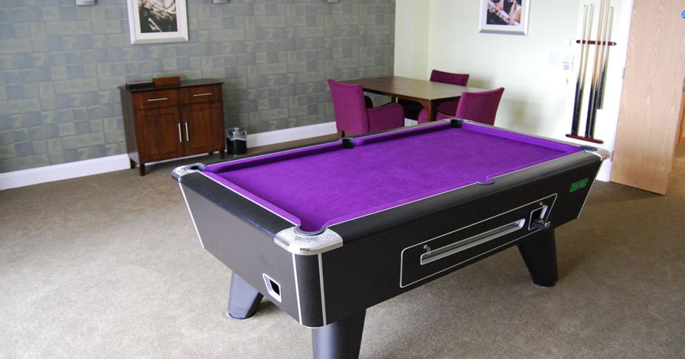 A good sized room with a purple quilted snooker table located centrally of a games room.