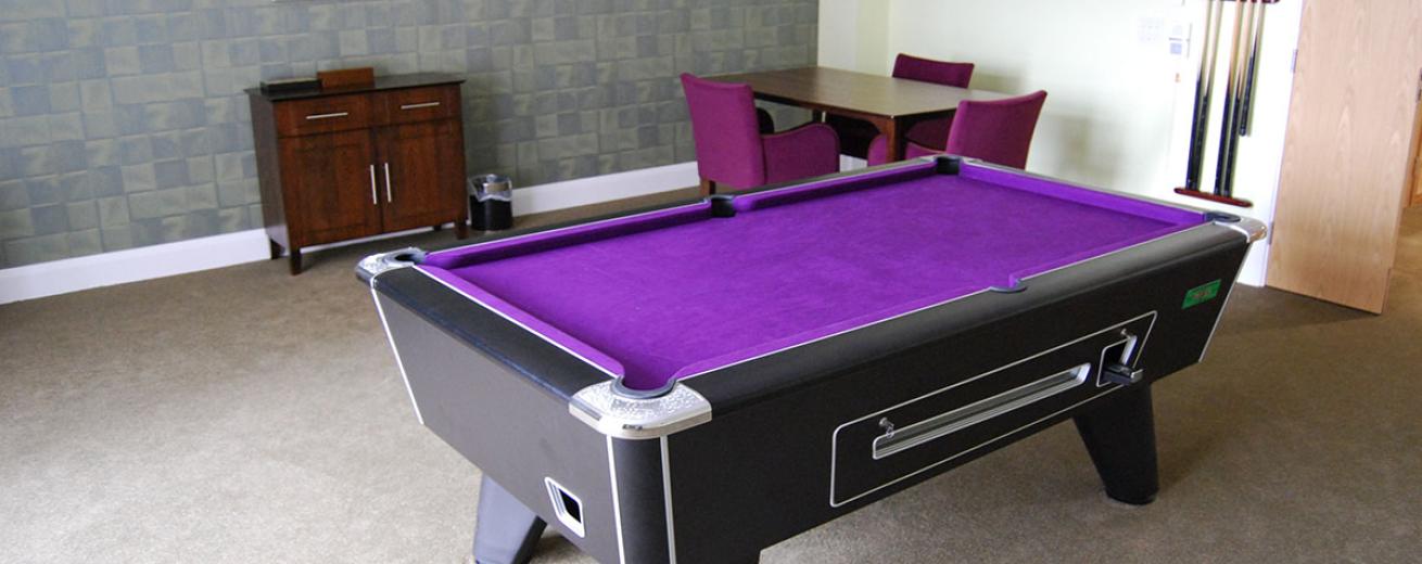 A good sized room with a purple quilted snooker table located centrally of a games room.