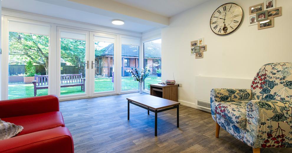 Large airy communal seating area, with masses of natural light flooding in from the wall of patio doors leading into the garden. The wooden floors soften the look of the room with decorative colourful armchair seating options.