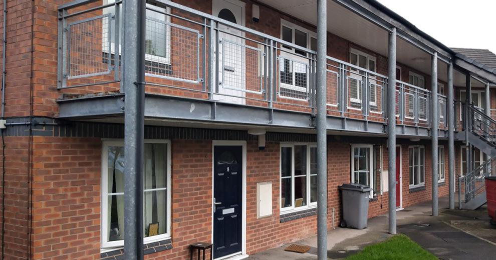 Industrial support metal beams and balcony on the second storey frame the entry to Thomas Court flats.