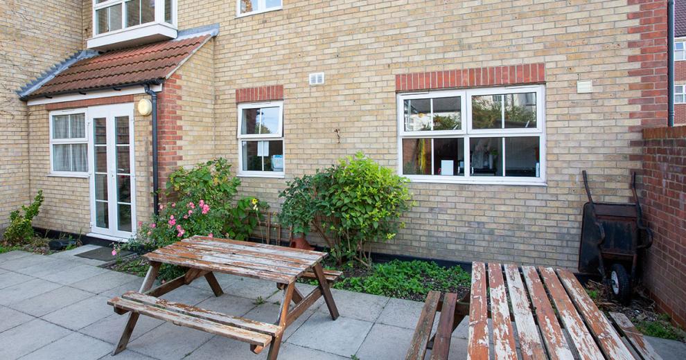 A compact patioed garden area with two wooden benched seating options.