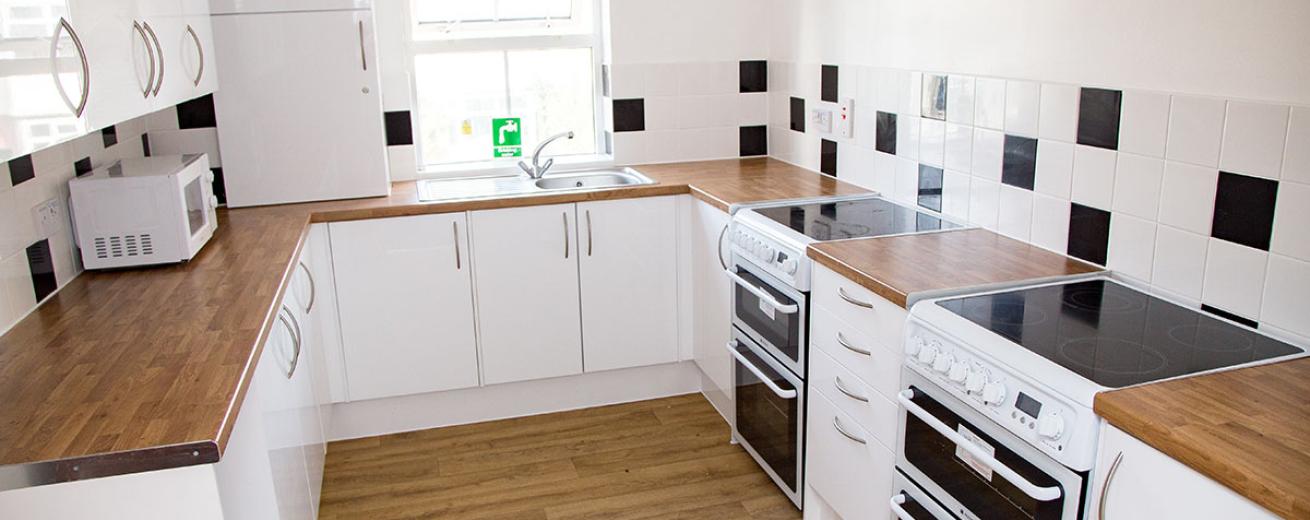The brilliant white kitchen cupboards and stark contrast of the wooden work top give the kitchen a clean and crisp feel. It hosts two white electric hob and oven, a microwave and kettle.