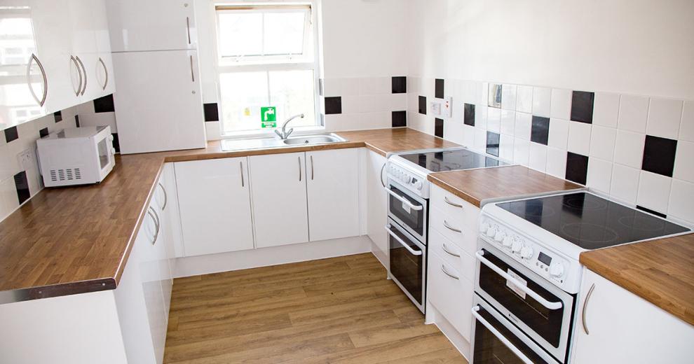 The brilliant white kitchen cupboards and stark contrast of the wooden work top give the kitchen a clean and crisp feel. It hosts two white electric hob and oven, a microwave and kettle.