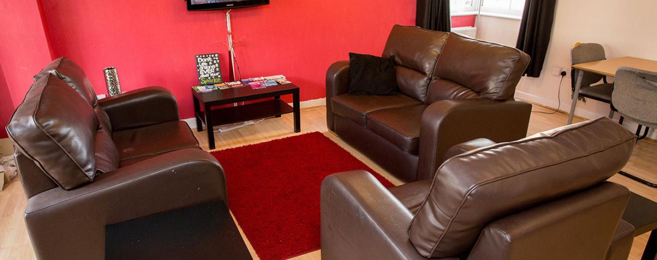 Dark, plush, two two-seater leather sofas encircling a small wall mounted television against a deep red painted wall.