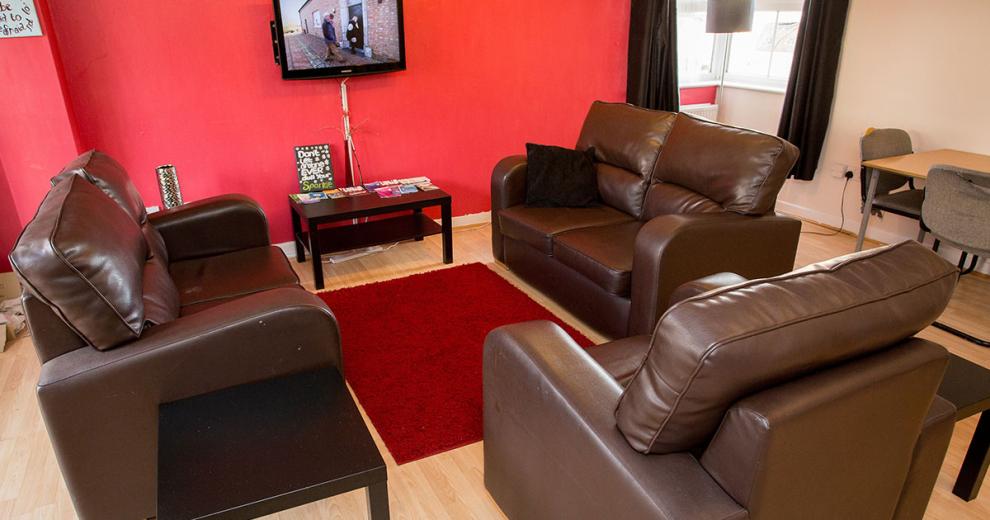 Dark, plush, two two-seater leather sofas encircling a small wall mounted television against a deep red painted wall.