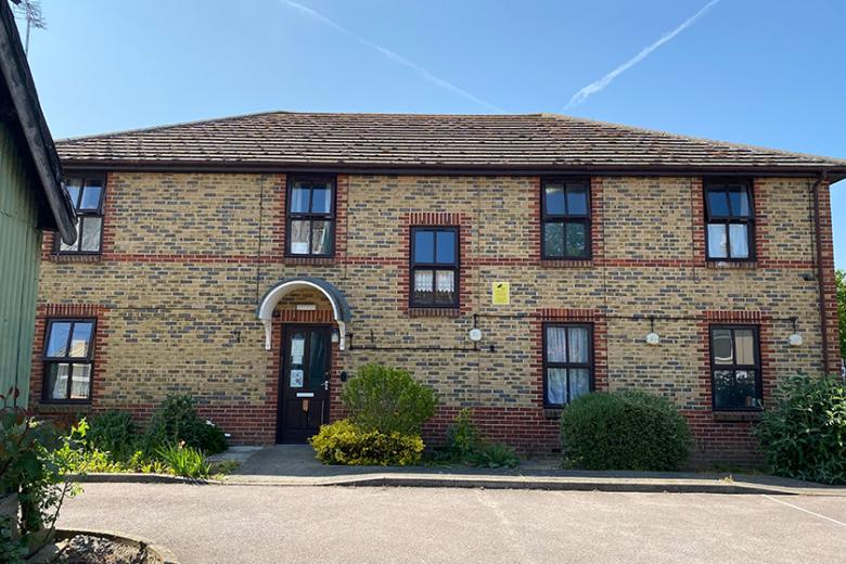 Traditional, elongated, two storey brown bricked property with decorative red brick design around the windows and entrance door. Small, well maintained shrubbery lines the perimeter of the property.