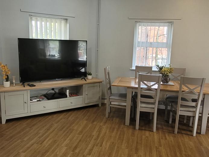 Cosy communal area with large screen TV, wooden dining table and chairs and wooden flooring