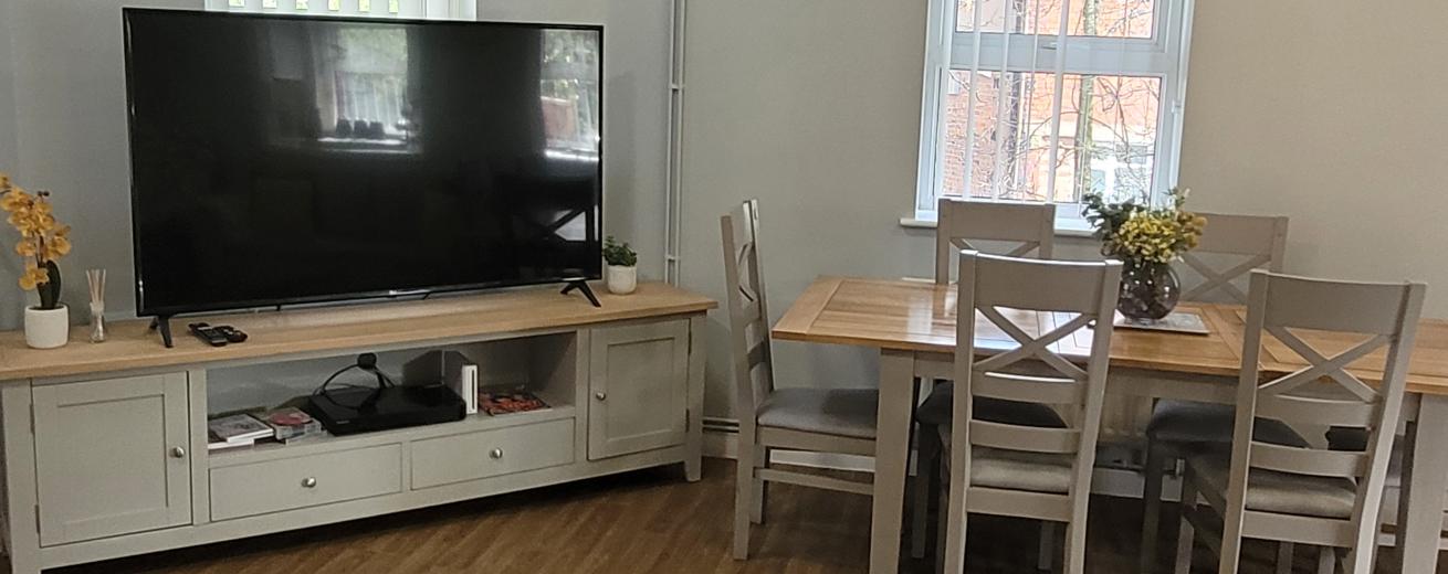 Cosy communal area with large screen TV, wooden dining table and chairs and wooden flooring