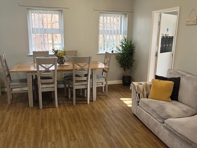Cosy communal area with grey sofa, wooden dining table and chairs and wooden flooring