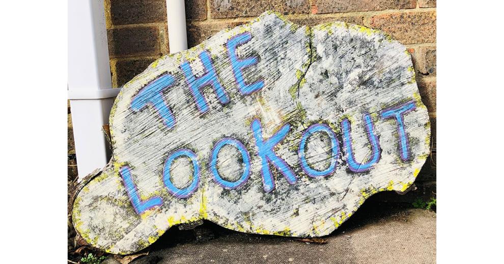 Large wooden block with the words The Lookout written on in blue paint and a purple outline.