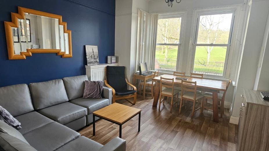 Spacious, elongated living and dining area decorated with a navy blue painted feature wall and white washed walls on the other. The room is divided with plush large leather sofas and a six person dining table in the other half of the room in front of the large bay window.