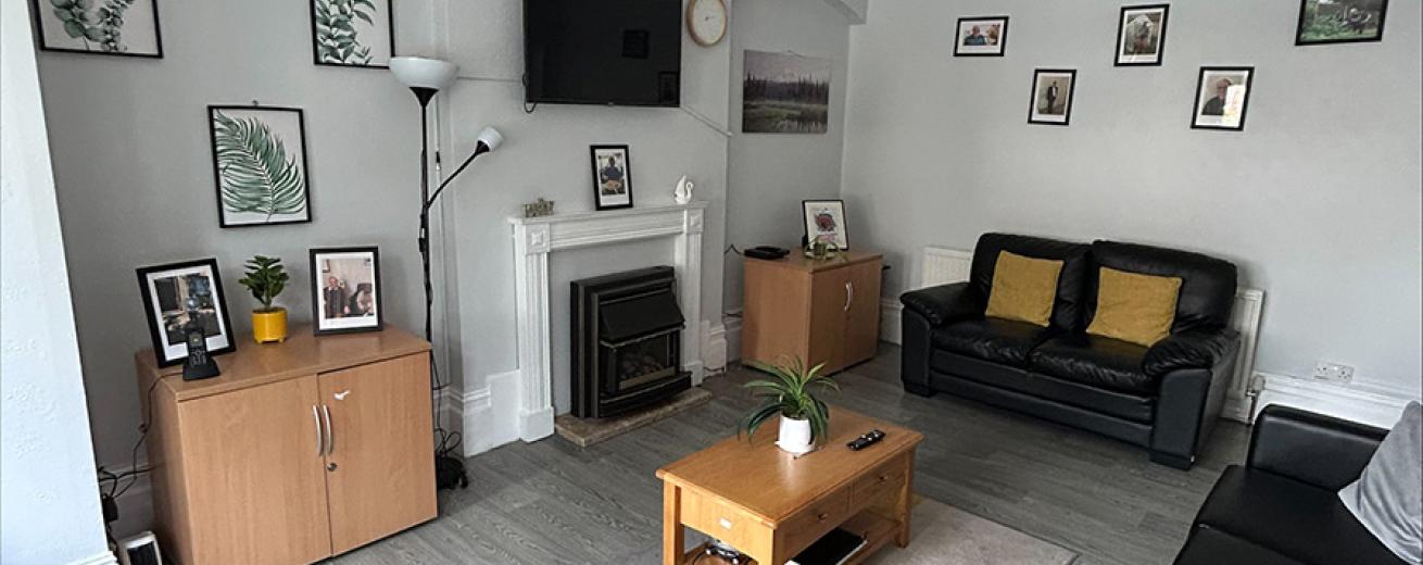 Plump black leather seating options on a laminate flooring and natural lighting coming from the large bay window.