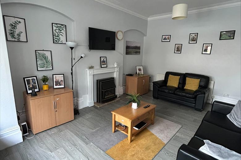 Plump black leather seating options on a laminate flooring and natural lighting coming from the large bay window.