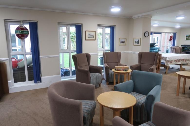 Bright residents' lounge with armchairs, tables and garden-facing windows