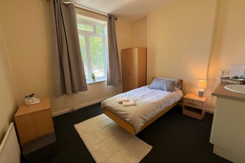Bright single bedroom with wardrobe, bedside table and large window at Primrose House.