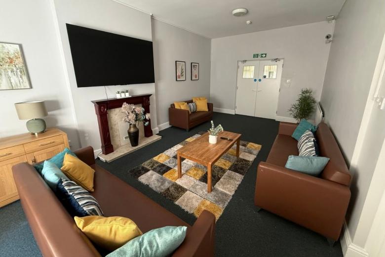 Comfortable communal lounge with sofas, coffee table and large wall-mounted TV at Primrose House.