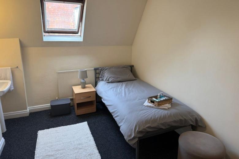 Single bedroom with skylight window, bedside table and en suite wash basin at Sandwood House.