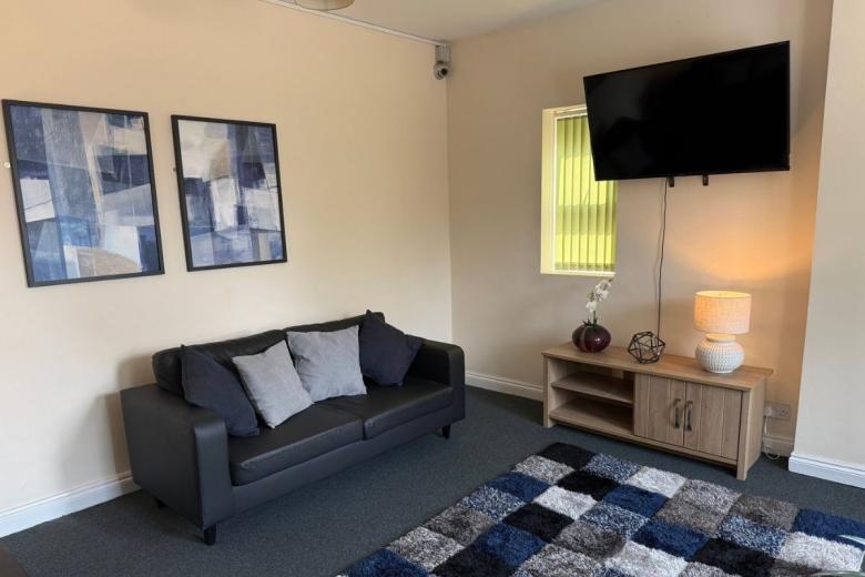 Comfortable communal lounge with sofa, wall-mounted TV and modern furnishings at Sandwood House.