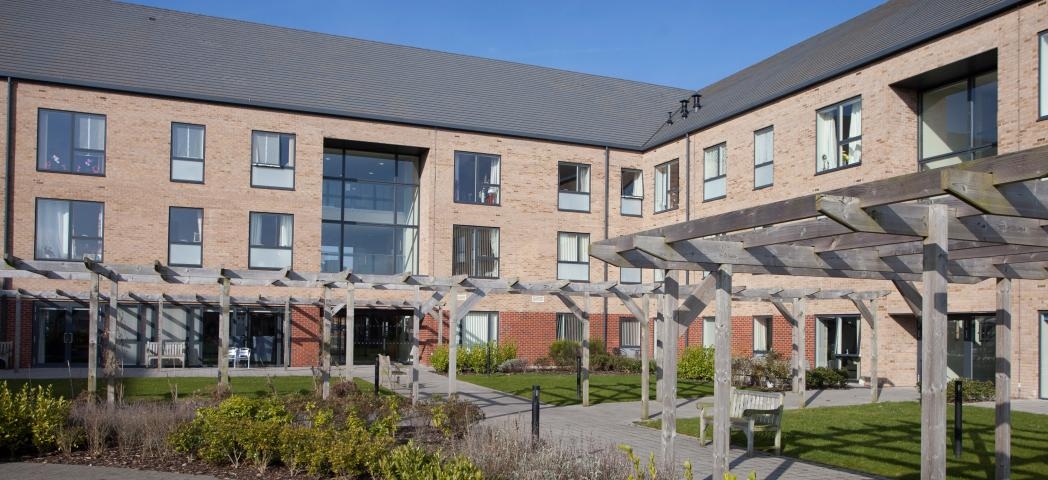 Stylized retirement living community with an array of large windows over looking a sectioned off grassed areas, flower beds and walkways, located in Stoke-on-Trent.