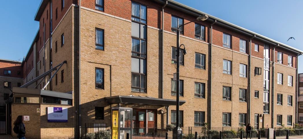 A four storey new-build brick apartment block, located by a main road with gated access to the entrance and a secure gated carpark. 