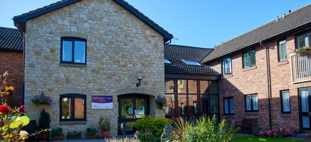 A stunning blend of stone materials for the façade of the entrance to Harry Garrett Court, the dark wooden framed window and doors contrast beautifully, to the left there is a wonderful floor to ceiling walkway linking to the traditional red brick extension. The well maintained gardens guide you to the entranceway in an inviting manner.