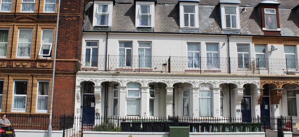 Ornate exterior of a three-storey whitewashed terraced supported housing property in Great Yarmouth. With second storey property width balcony.