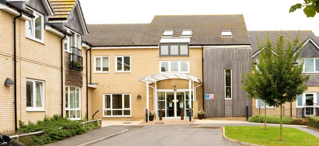 A modern two storey property built with yellow brick and a wooden panelling in random locations on the exterior of the property. The entrance has a covered walkway and dropped curb access. 