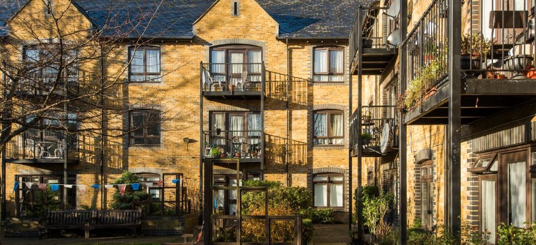 Traditional yellow bricked property with grey bricked framing around the windows and doorways. Iron barred balconies are attached to the large curved toped patio doorways. Wheelchair access pathways run around the perimeter of the building.