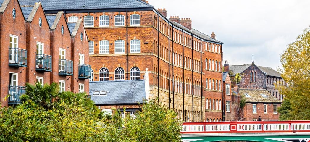 Riverside view of Kelham Island museum in Sheffield, and colourful green, red and white bridge spanning the river. 