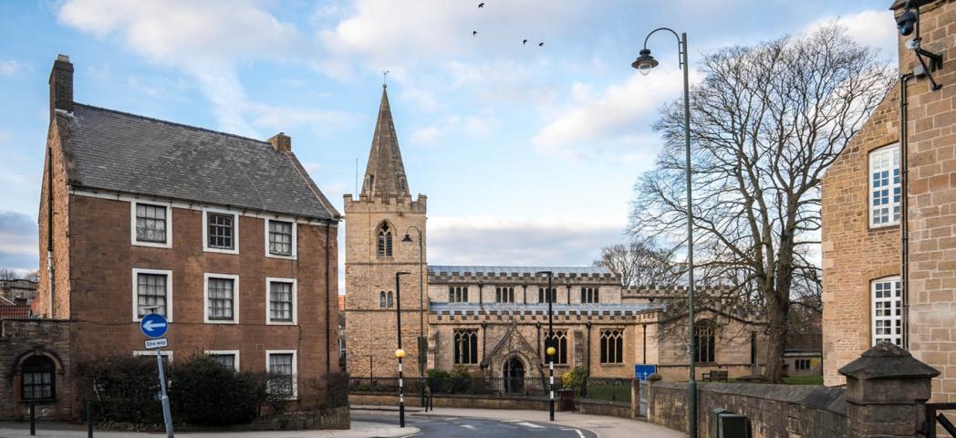 St Peters Church in Mansfield town centre with vicarage and one way road passing through village.
