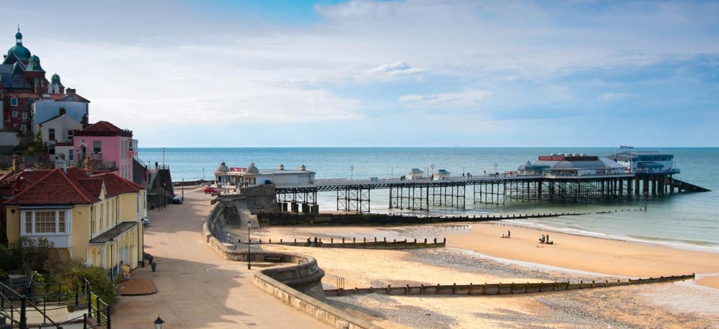 Large promenade walkway leading to a modern pier which features over a mixture of sand and stone beach and into the North Sea.