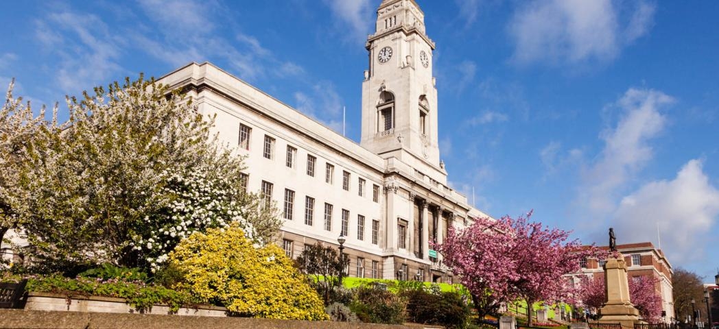 Stone built town hall with well-maintained gardens in bloom.