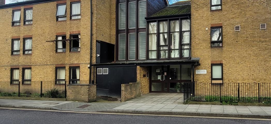Traditional yellow brick built apartment block, featuring dark brown wooden panelling on the entrance elevation and window panes. 