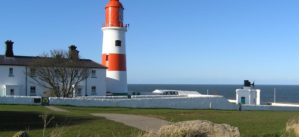 Picturesque red and white striped lighthouse on the edge of the cliff face, behind sits numerous joined buildings to facilitate the lighthouse.