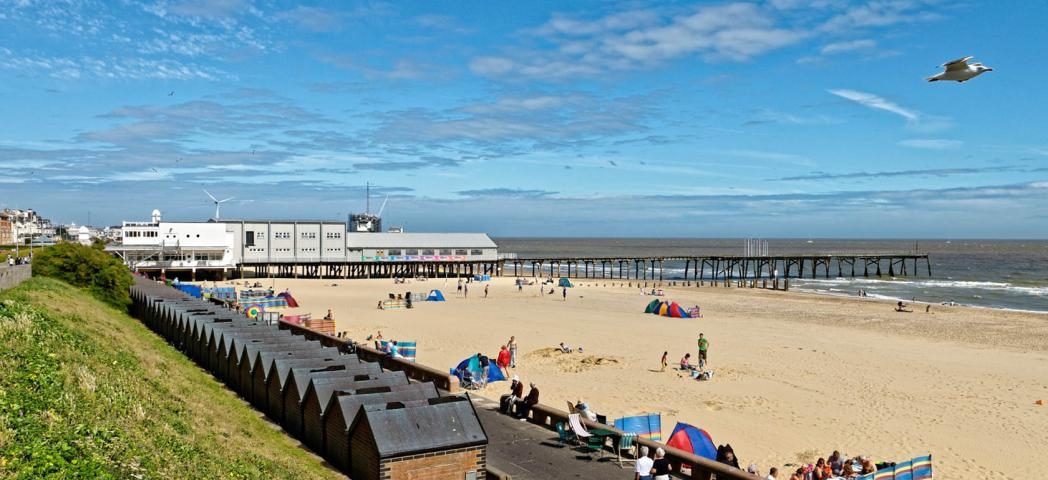 Golden sandy beach, sectioned off by a short pier. The small bricked beach huts line the promenade.