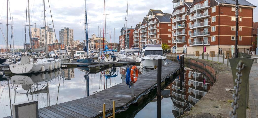 Multiple docked yachts on the waterfront with the city skyline in the distance and modern apartments built around the waters edge.