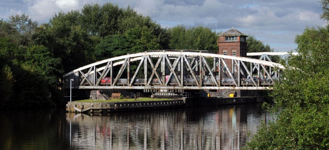 Weathered silver, curved metal bridge creating access over the river.