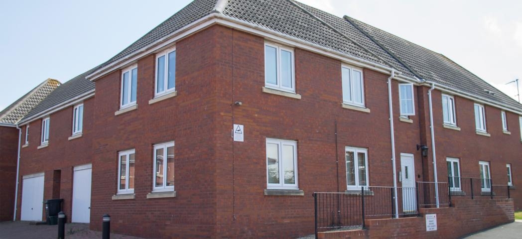 New build, red brick corner plot with new white PVC windows, doors and garage. A bricked wall surrounds the walkways. 