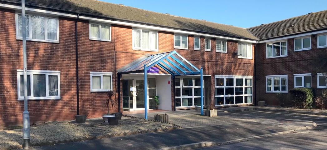 Two storey red bricked right angle built building. The entranceway has a pop of blue within the sheltered area before the property, dropped curb access is located in front of the property.