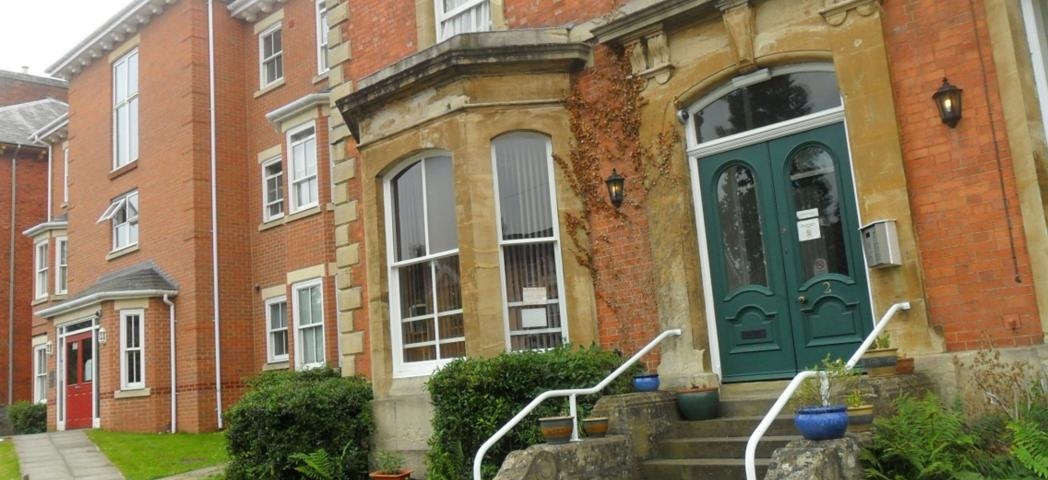 Victorian styled, three storey property with protruding bay windows and an array of forest green and red double entrance doors. 